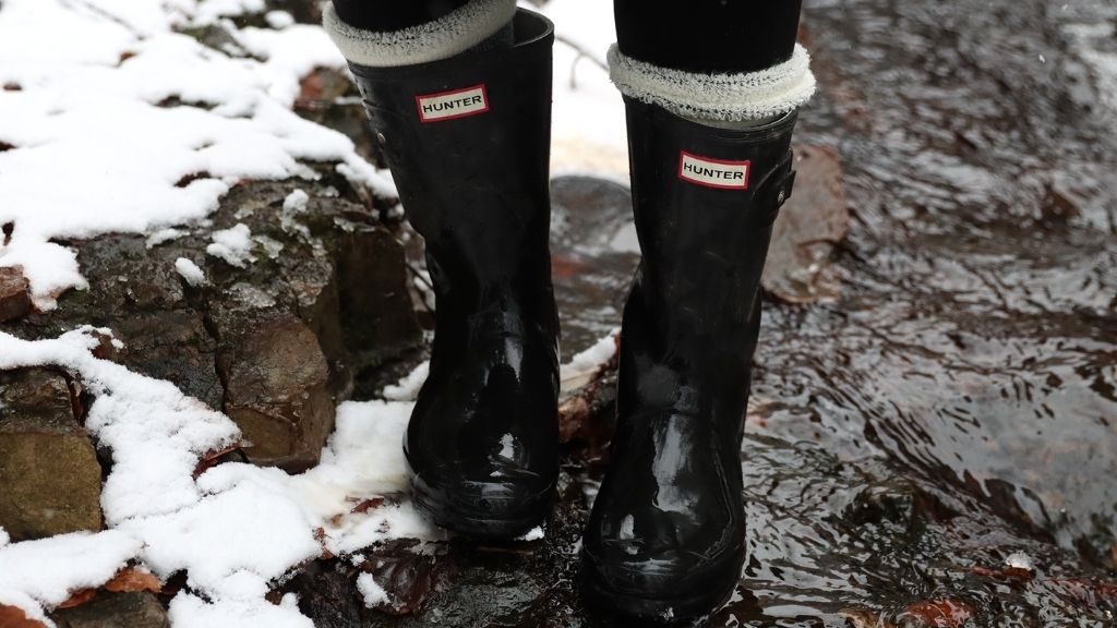 Svarta gummistövlar som står i forsande vatten med snö i vattenbrynet