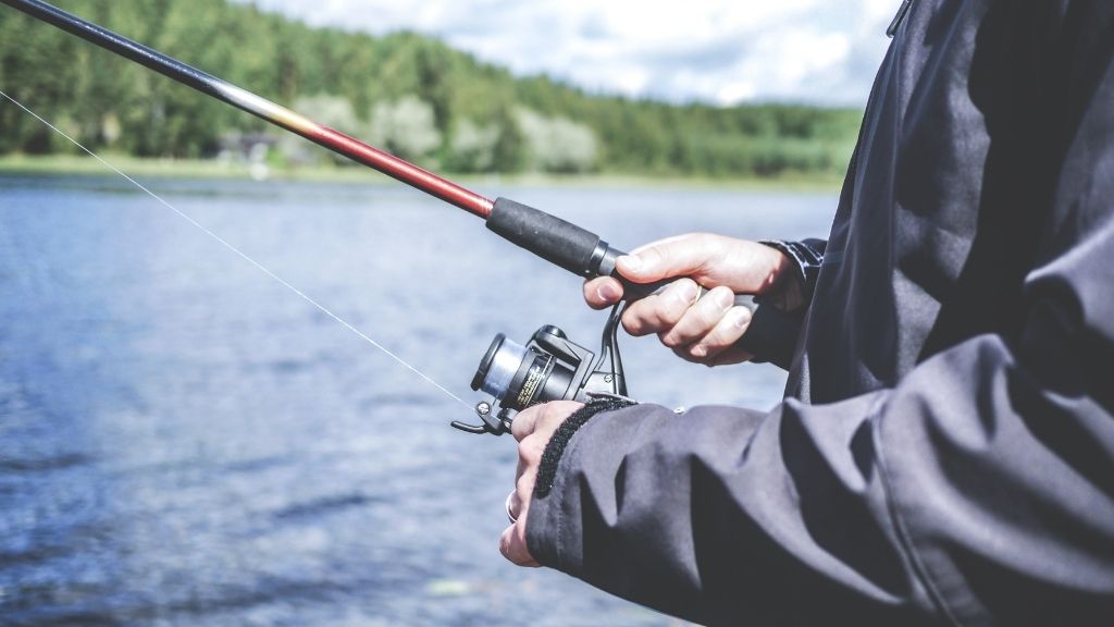 Närbild på ett par händer som håller i ett fiskespö med vatten i bakgrunden