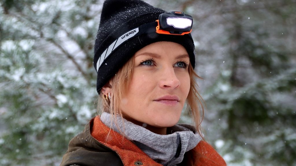 Kvinna med mössa som bär en lysande pannlampa med vinterlandskap i bakgrunden