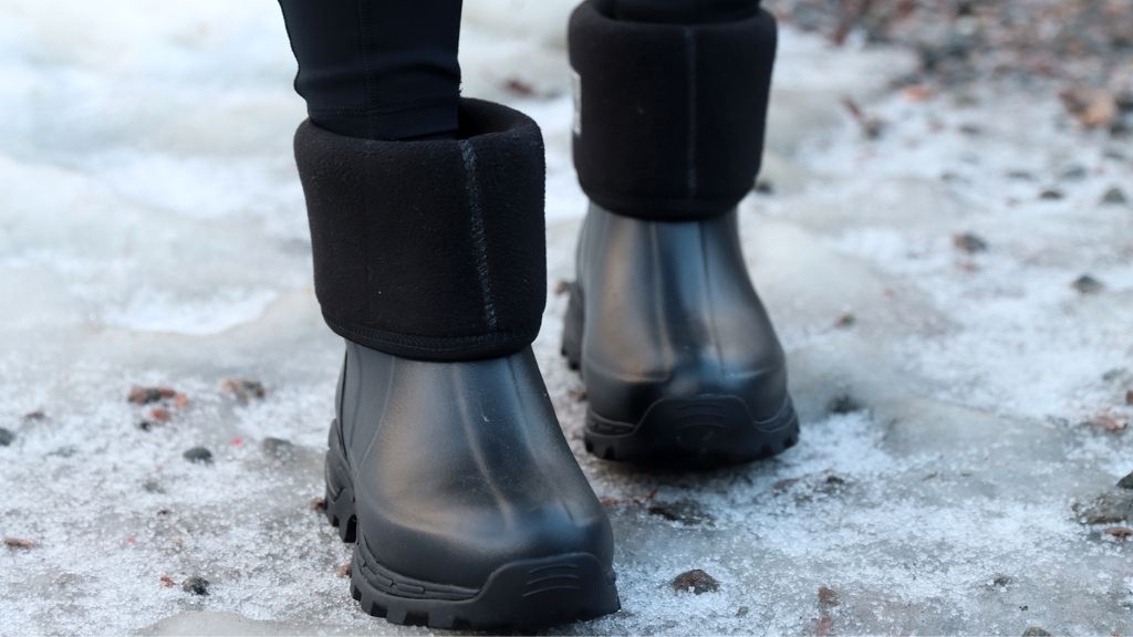 Svarta fodrade gummistövlar med nedvikt kant som står på snöigt och isigt underlag
