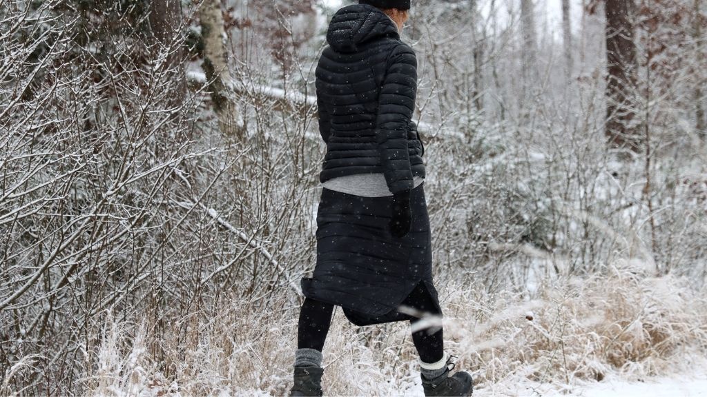 Person som bär svart täckkjol och svart täckjacka går i snötäckt skog